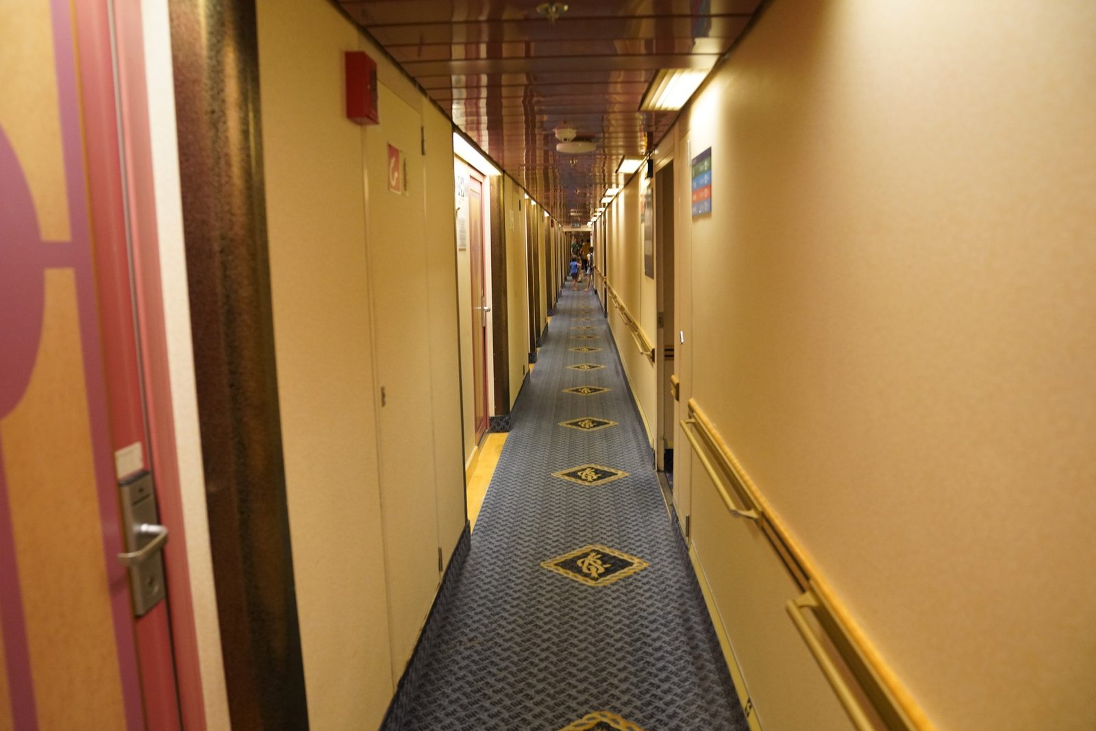 Corridoio lungo e stretto del traghetto, con porte di cabine da entrambi i lati e una moquette blu a rombi dorati