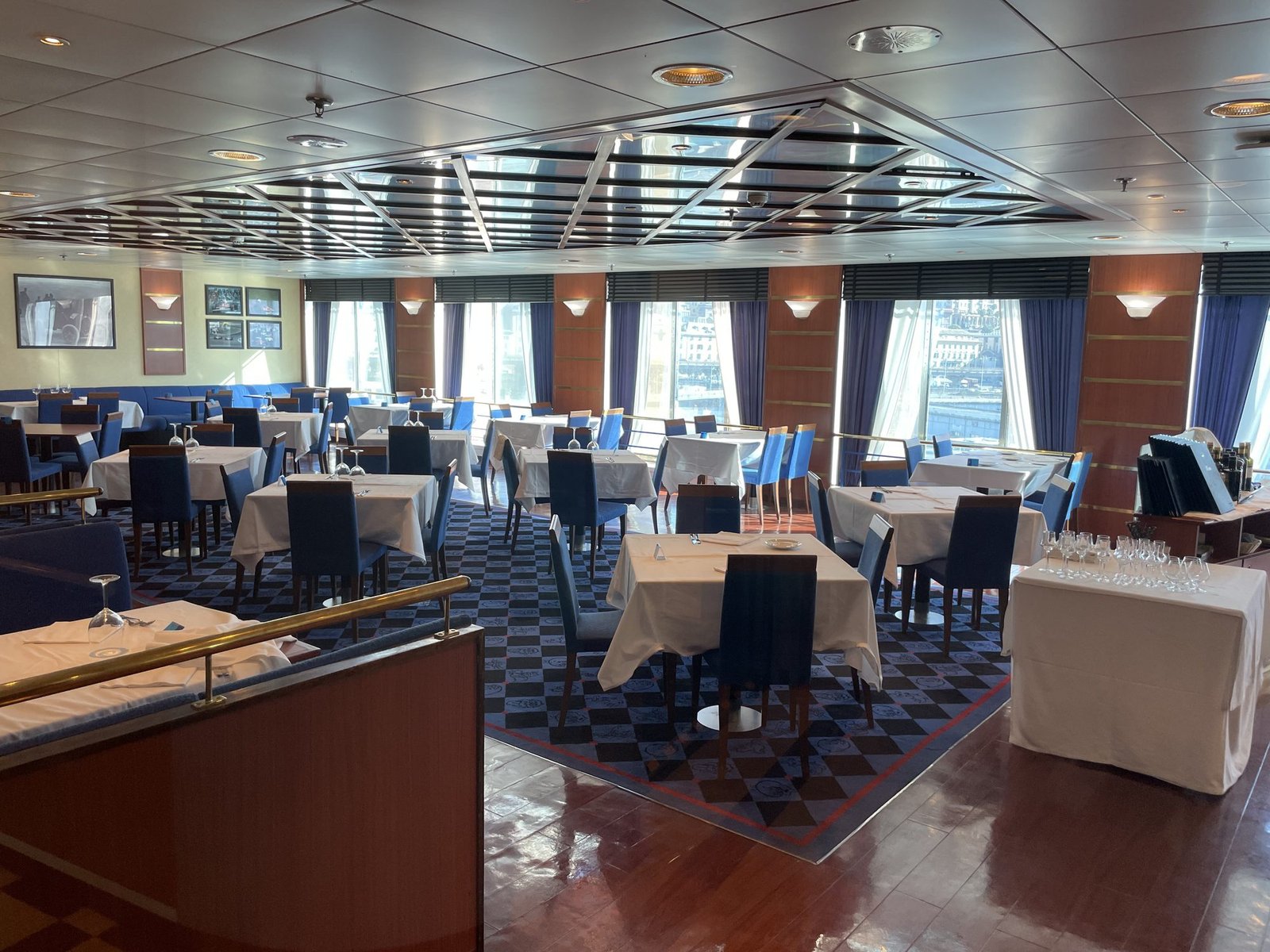 Il ristorante a bordo con tavoli apparecchiati con tovaglie bianche, sedie blu e finestre con le tende blu che danno sulla città di Genova