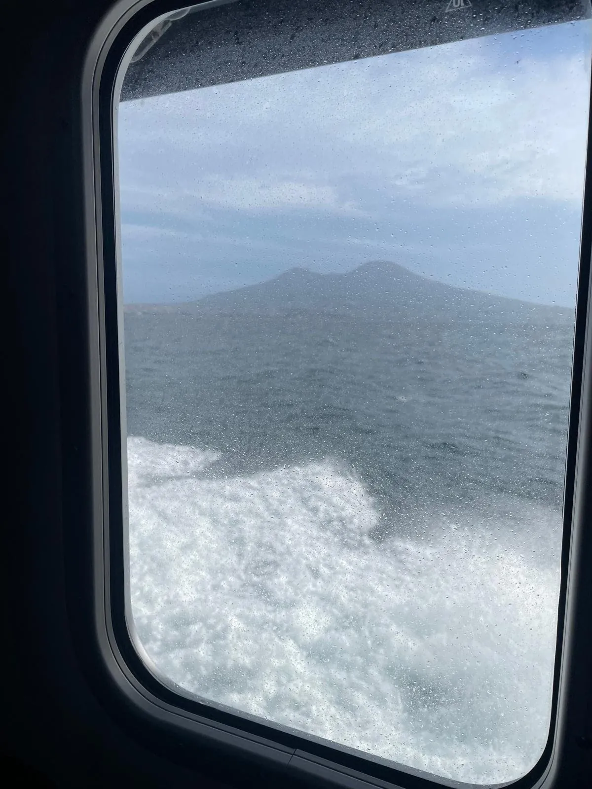 Il Vesuvio visto dal finestrino bagnato dell’aliscafo, con la schiuma del mare sotto